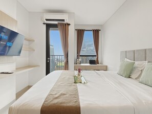 A hotel room with a bed, a TV, a desk with a laptop, and a view of the city. - Homey Wooden Touch Studio At Apartment Ciputra World 2 (Jakarta)