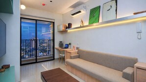 Un salón moderno con un sofá, una mesa de centro, un escritorio con una computadora portátil y un ventanal con vistas a la ciudad.