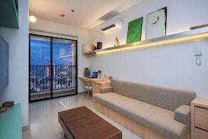 Un salón moderno con un sofá, una mesa de centro, un escritorio con una computadora portátil y un ventanal con vistas a la ciudad.