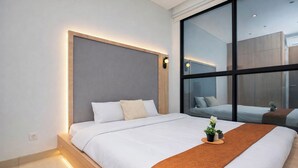 Una habitación de hotel moderna con una cama grande, una mesita de noche, una ventana y vistas a la ciudad.