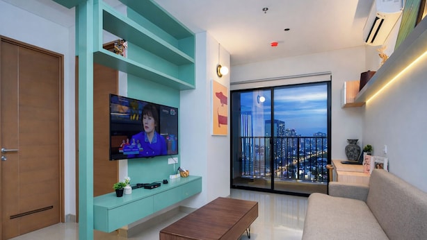 Una sala de estar moderna con un televisor de pantalla plana, un sofá, una mesa de centro y vistas a un paisaje urbano a través de un ventanal grande.