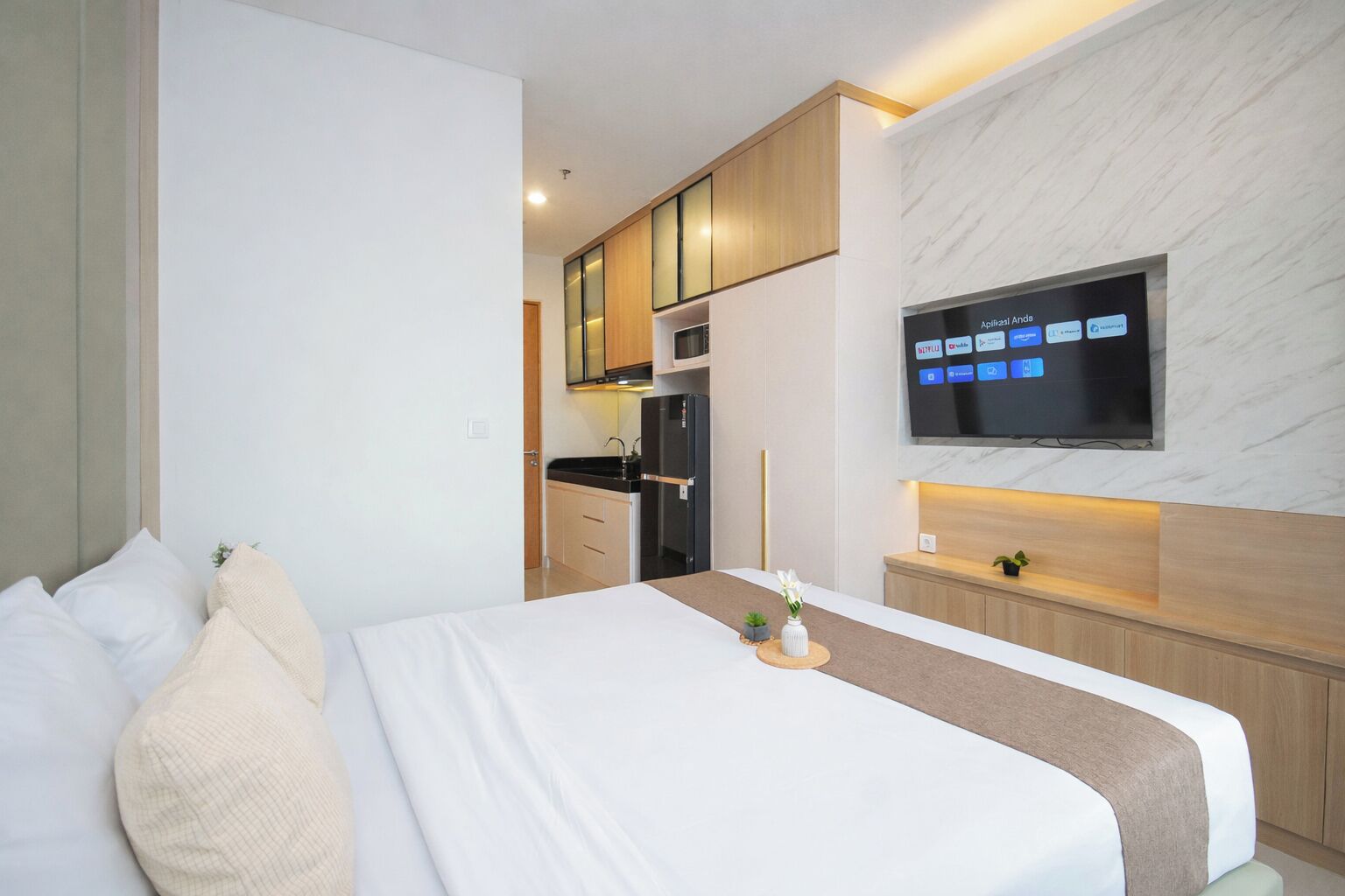 Une chambre d’hôtel comprenant un lit, un téléviseur fixé au mur, un petit coin cuisine et un meuble en bois.