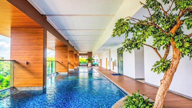 A long indoor swimming pool with wooden pillars, a potted tree, and a clear view of the outdoors. - Chic And Warm Studio With Super King Bed At Capitol Suites Apartment (Jakarta)