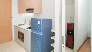 A compact kitchen with a refrigerator, sink, oven, and a wooden door. - Chic And Warm Studio With Super King Bed At Capitol Suites Apartment (Jakarta)