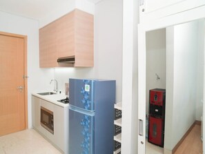 A compact kitchen with a refrigerator, sink, oven, and a wooden door. - Chic And Warm Studio With Super King Bed At Capitol Suites Apartment (Jakarta)