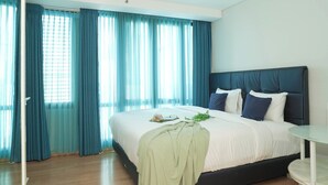 A bedroom with a bed, a bedside table, and a window with curtains. - Chic And Warm Studio With Super King Bed At Capitol Suites Apartment (Jakarta)