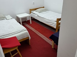 A room with two single beds, a small white table, a red carpet, and a wooden bench.
