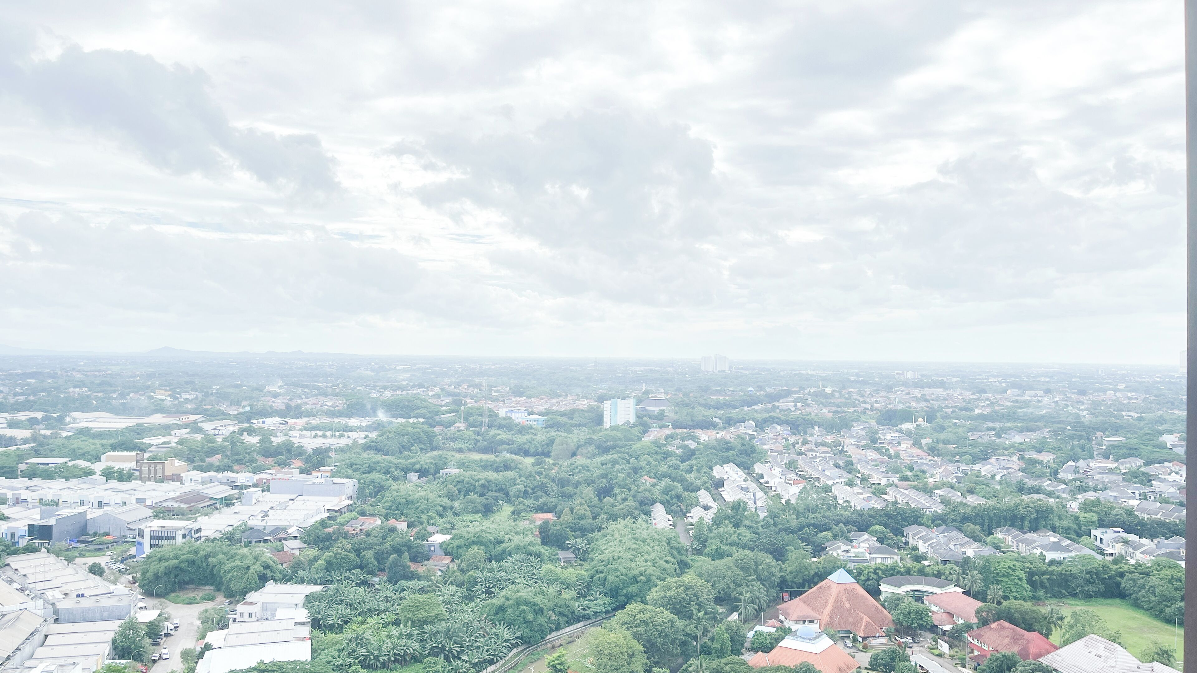 A cityscape with a mix of residential and commercial buildings, a prominent church, and a distant mountain range under a cloudy sky.