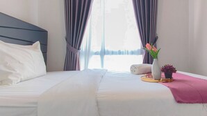 Una cama bien hecha con sábanas blancas, cabecera oscura y una manta rosa.