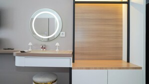 A modern bathroom with a round mirror, two small lamps, a vanity, and a stool. - Chic Brown Touch Studio At Apartment Collins Boulevard (Tangerang)