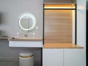 A modern bathroom with a round mirror, two small lamps, a vanity, and a stool. - Chic Brown Touch Studio At Apartment Collins Boulevard (Tangerang)