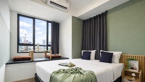 A hotel room with a large bed, a window with curtains, a bedside table with a lamp, and a view of the cityscape. - Bright And Relaxing 2Br At Collins Boulevard Apartment (Tangerang)