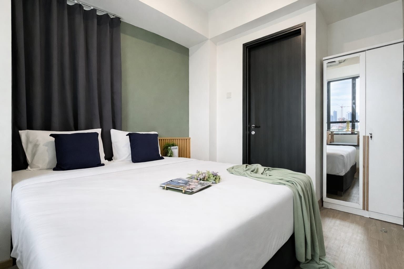 A hotel room with a bed, a nightstand, a mirror, and a door leading to another room.