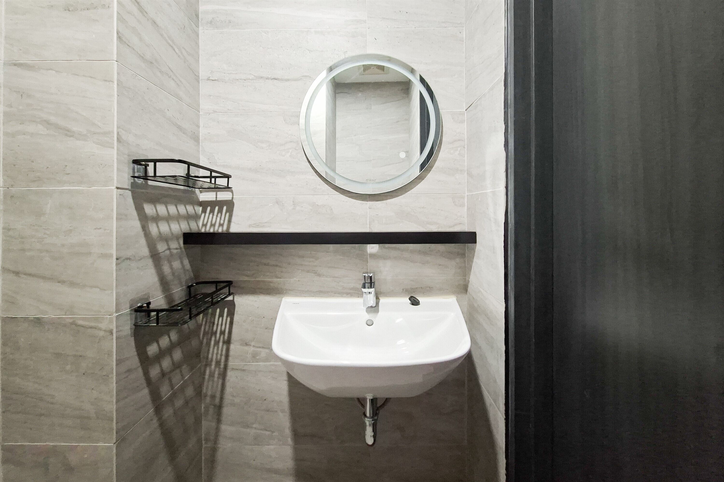 Un bagno con un lavandino bianco, uno specchio rotondo e un portascopevoli.