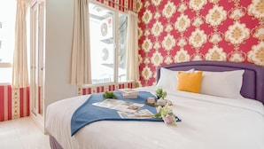 A hotel room with a bed, a window with curtains, a patterned wall, and a ceiling fan. - Classic Red Studio At Nifarro Park Apartment (Jakarta)