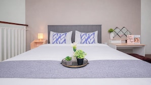 A neatly made bed with a grey headboard, a bedside table with a lamp, and a tray with flowers and a small plant. - Stunning Studio Loft At Nifarro Park Apartment (Jakarta)