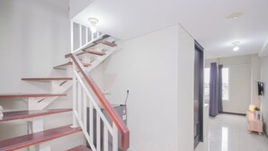 A staircase with wooden steps and white railings, a flat floor, a wall-mounted TV, and a small table with a plant. - Stunning Studio Loft At Nifarro Park Apartment (Jakarta)