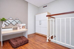 Une pièce avec un plancher en bois, une armoire blanche, un bureau avec un miroir, un coussin marron et une rambarde blanche.