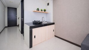 A compact kitchen with a black countertop, a sink, and a small shelf with plants. - Stunning Studio Loft At Nifarro Park Apartment (Jakarta)