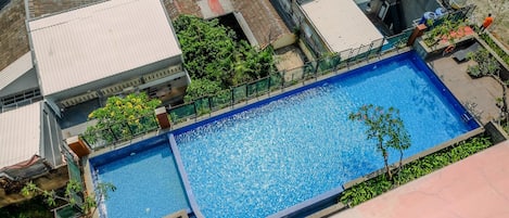 Eine Vogelperspektive auf einen Swimmingpool, umgeben von Gebäuden, mit blauem Himmel.