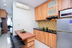 Eine kleine Küche mit Holdekor-Schränken, einer schwarzen Arbeitsplatte, einem Edelstahl-Kühlschrank und einer gefliesten Rückwand.