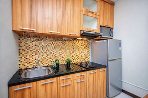Eine Küche mit Holzschränken, einem Edelstahlspülbecken, einem Kühlschrank und einer gefliesten Rückwand.