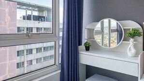 Ein Zimmer mit einem großen Fenster, einem runden Spiegel, einem weißen Konsolentisch und Blick auf Gebäude und eine Brücke.