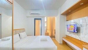 Ένα δωμάτιο ξενοδοχείου με ένα κρεβάτι, μια τηλεόραση, έναν καθρέφτη και ένα παράθυρο με κουρτίνες.