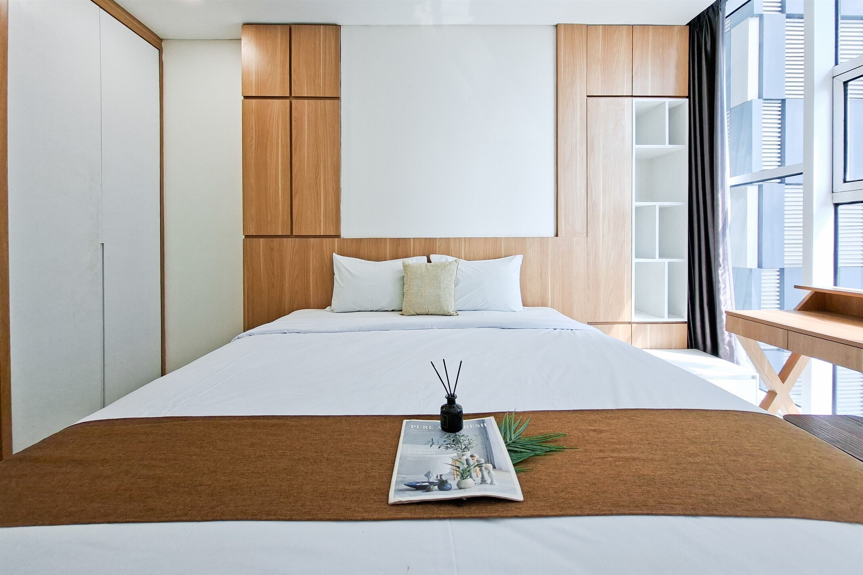 A modern hotel room with a large bed, wooden headboard, and a desk with a chair.