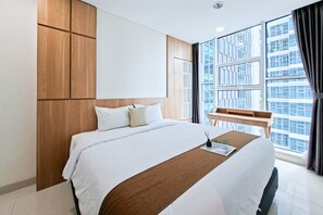 Ein Hotelzimmer mit einem großen Bett, einem Schreibtisch und Blick auf eine Stadtkulisse durch große Fenster.