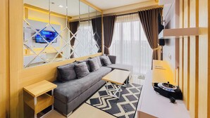 A modern living room with a sofa, TV, and a patterned rug. - Neat Warm Wooden Tone 1Br At Patraland Amarta Apartment (Ngaglik)