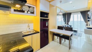 A modern kitchen with a built-in stove, a sink, and a dining area with a table and chairs. - Neat Warm Wooden Tone 1Br At Patraland Amarta Apartment (Ngaglik)