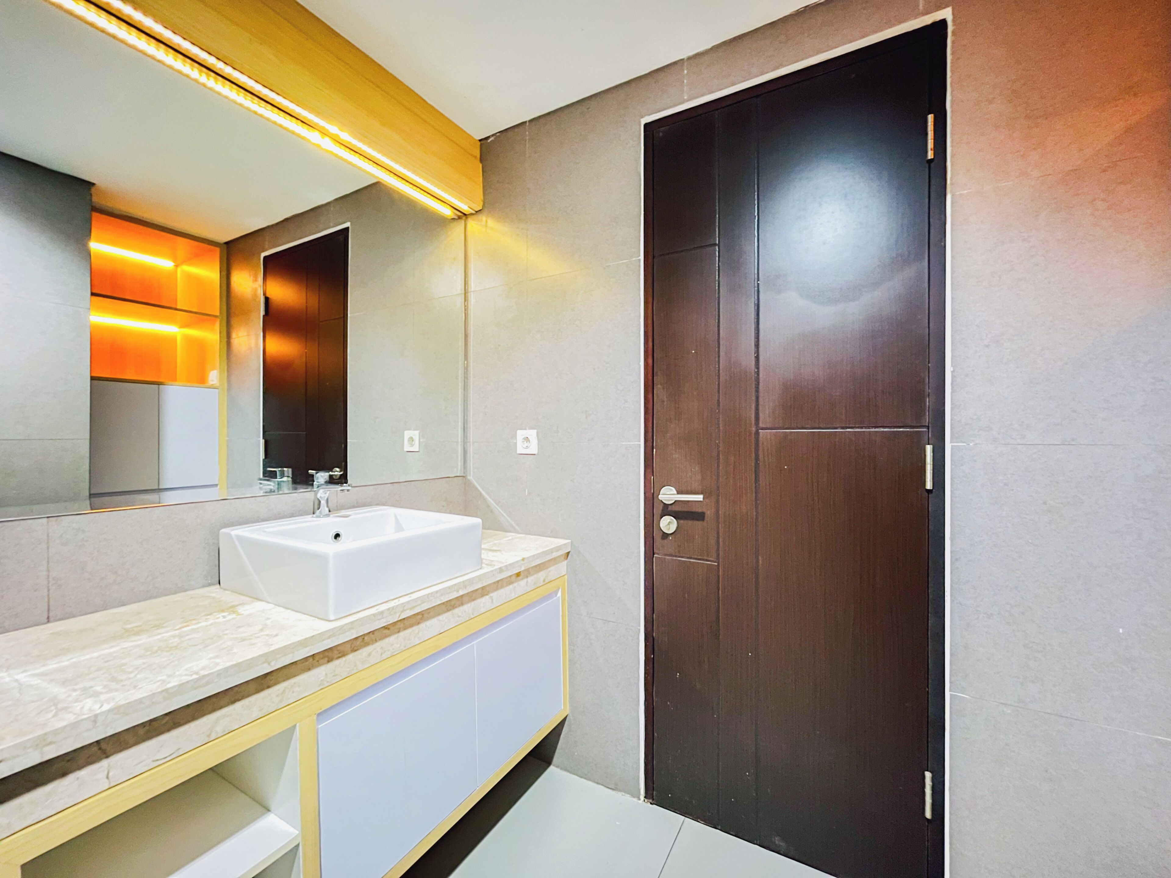 A modern bathroom with a white sink, mirror, and wooden door.