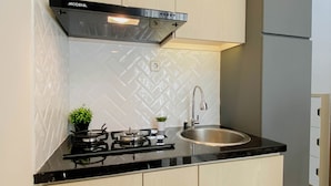 A modern kitchen with a gas stove, stainless steel sink, and a hood above the stove. - Practical 2Br For 4 Pax At Podomoro Golf View Apartment (Gunung Putri)