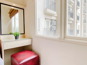 Ein Badezimmer mit Spiegel, einer Topfpflanze, einem roten Hocker und einem Fenster mit Blick auf Balkone.