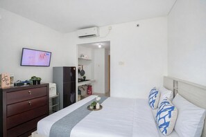 Quarto de hotel com cama, cômoda, televisão, frigorífico e área de cozinha.