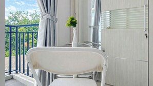 A balcony with a white chair, a small potted plant, and a view of trees and sky. - Classic White Studio At Apartment Woodland Park Residence (Jakarta)
