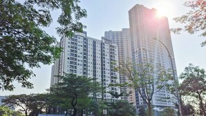 A high-rise building with multiple floors, surrounded by trees and a road with parked cars. - Cozy Living 1Br Apartment At Silkwood Residence (Tangerang)