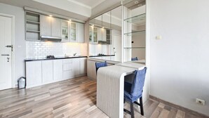 A modern kitchen with wooden cabinetry, a built-in island, and a dining area with a chair. - Cozy Living 1Br Apartment At Silkwood Residence (Tangerang)