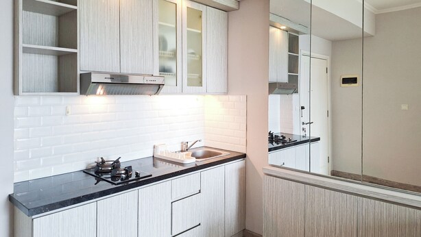 A modern kitchen with white cabinetry, a black countertop, and a stainless steel range hood. - Cozy Living 1Br Apartment At Silkwood Residence (Tangerang)