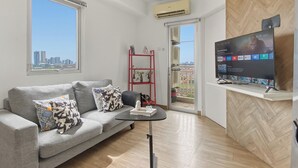 Un soggiorno moderno con un divano grigio, un tavolino nero, una TV su un mobile e uno scaffale rosso con oggetti decorativi.