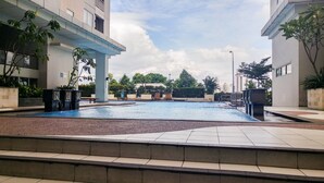 Una piscina con lettini, circondata da edifici moderni e vegetazione.