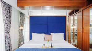 Habitación de hotel con una cama grande, cabecera azul, ropa de cama blanca, mesita de noche con bandeja y un armario con espejo.