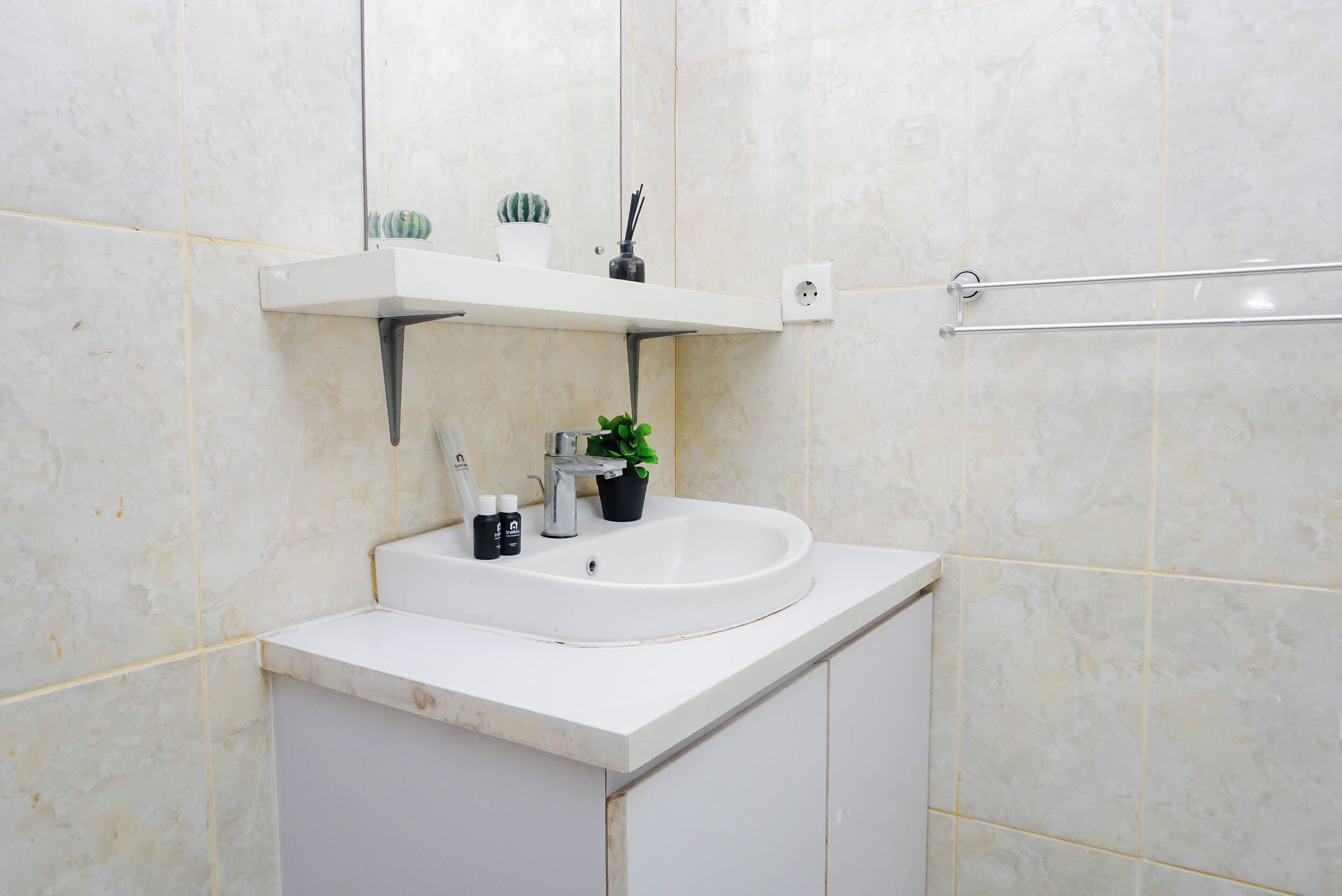 Une salle de bain avec un lavabo blanc, un miroir, une étagère contenant des articles de toilette et un porte-serviettes.