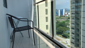 Ein Balkon mit Stuhl, Glastrennwand und Blick auf eine Stadtlandschaft mit Gebäuden und Grünflächen.