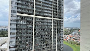 Um edifício residencial alto com várias varandas, janelas amplas e vista para um rio e a cidade ao redor.