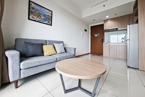 Un salon moderne avec un canapé gris, une table ronde en bois, une cuisine dotée de meubles en bois et un tableau encadré accroché au mur.