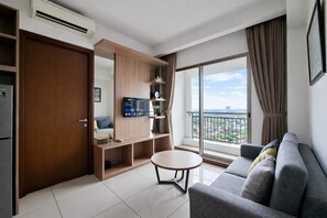 Un salon moderne avec un canapé, une petite table ronde, un téléviseur et un balcon offrant une vue agréable.