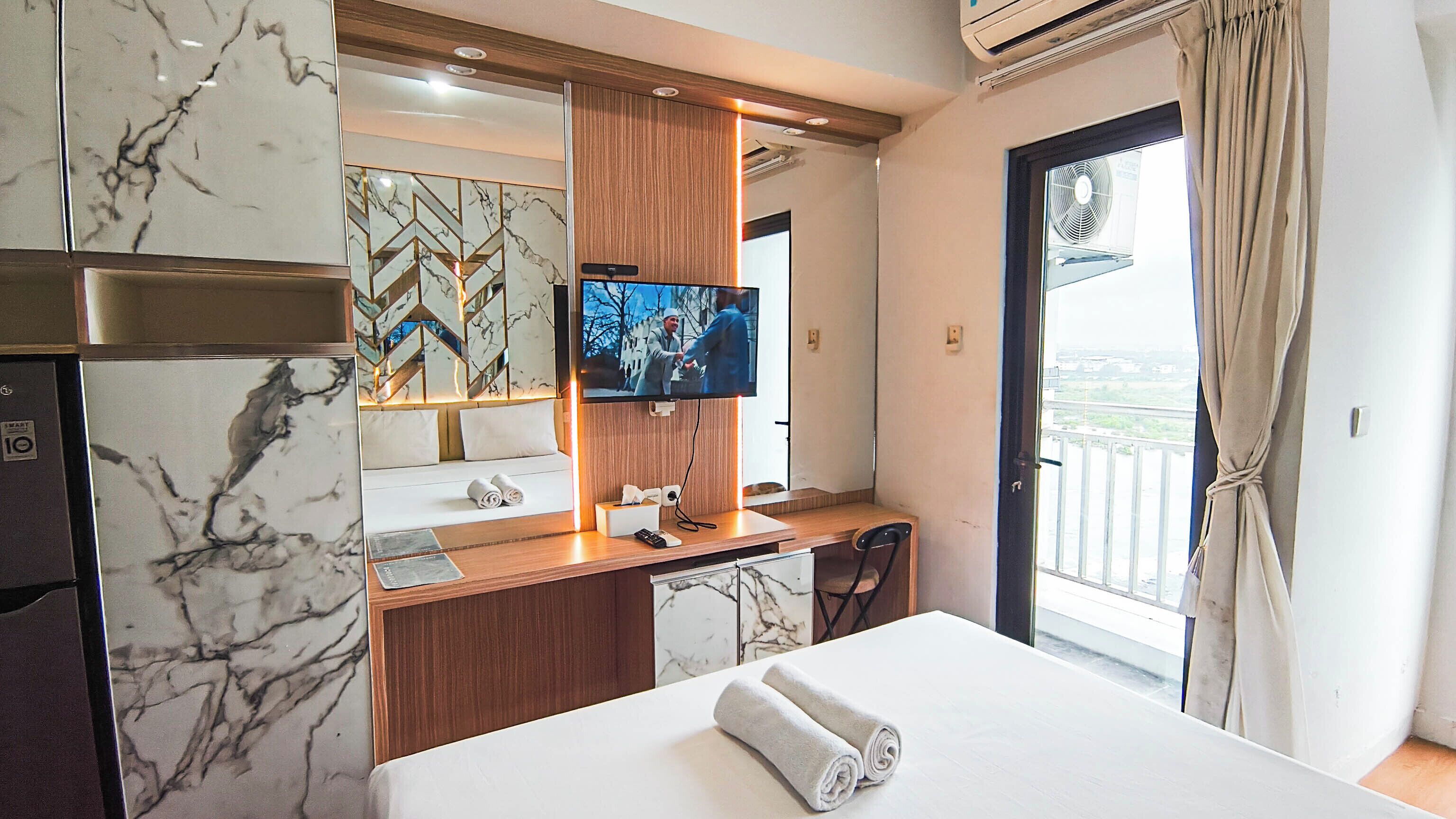 Een hotelkamer met een bed, een bureau met een televisie, een minibar en uitzicht op een balkon.