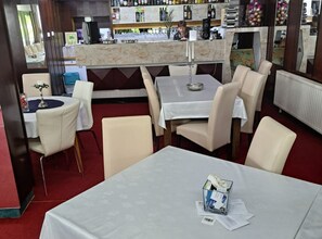Un restaurante con mesas y sillas, una zona de bar con botellas y vasos, y vistas al exterior.